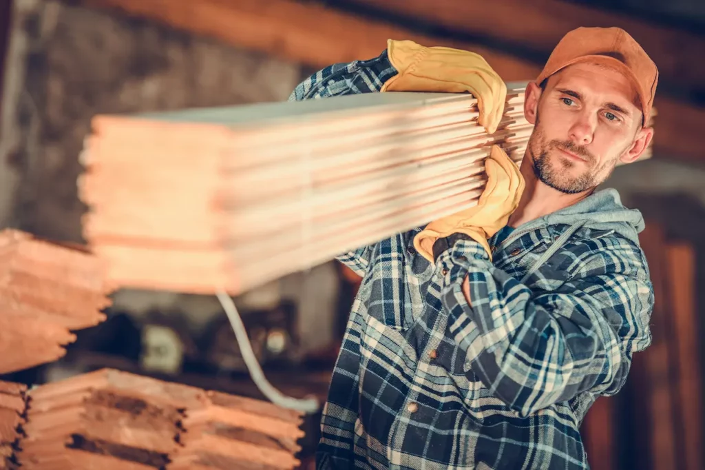Un homme porte une pile de planches de bois dans la cadre d’une livraison de matériaux de construction à Montréal