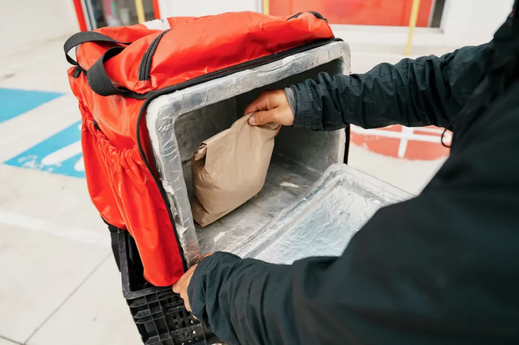 Livreur plaçant un colis dans un sac de livraison isotherme rouge à l'extérieur 